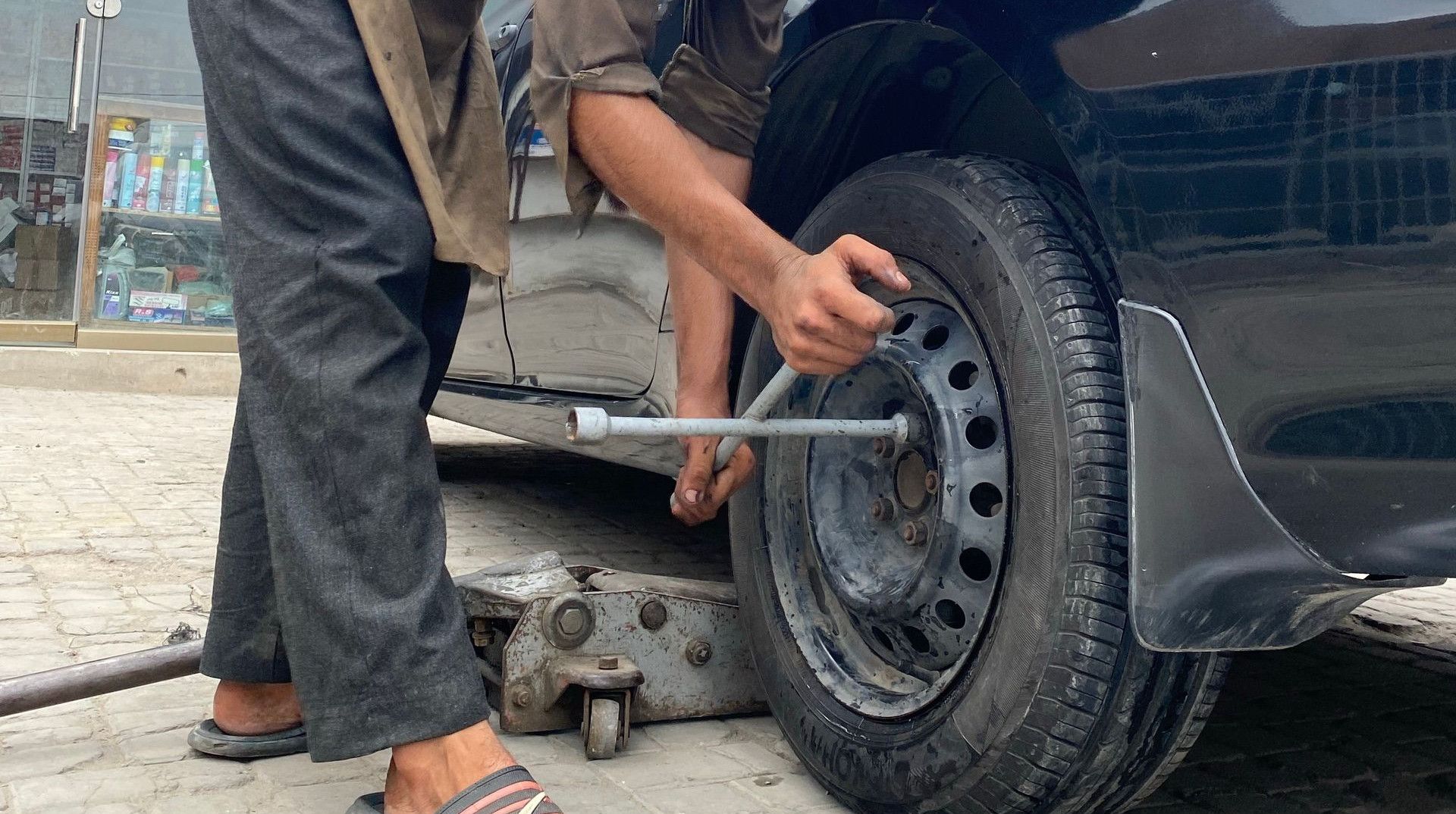 Young man repairing car wheel outdoors, showcasing automotive skills.